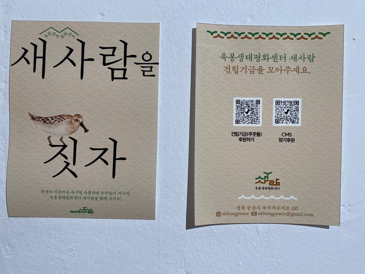 홍보물의 앞 뒤 면을 나란히 놓아두고 촬영한 사진이다. 왼쪽에 놓인 앞면에는 '옥봉생태평화센터 새사람을 짓자. 군산의 작은마을 옥서면 옥봉리에 우리들의 서식지, 옥봉평화센터 새사람을 함께 지어요!' 등의 문구가 적혀있고 오른쪽에 놓인 뒷면에는 '옥봉생터평화센터 새사람 건립기금을 모아주세요'라는 문구와 후원하기 QR 코드 등이 있다. 
