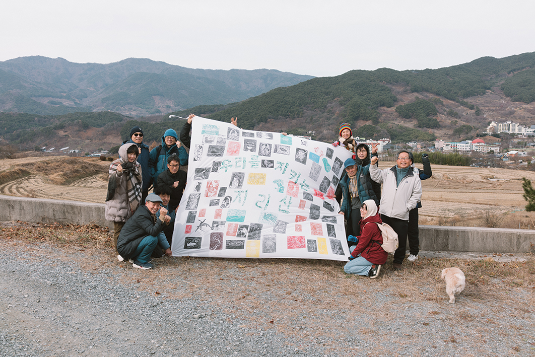 뒤로 논과 마을, 산이 보이는 공터에서 약 13명의 사람들이 커다란 현수막을 들고 정면을 바라보며 웃음을 지으며 서거나 앉아있는 모습을 촬영한 사진이다. 가로가 조금 더 긴 직사각형 모양의 현수막에는 가운데에 초록색으로 '우리를 지키는 지리산'이라는 문구가 있고 주변에는 지리산에서 살아가는 여러 생명들의 모습을 담은 작은 판화가 빼곡하게 찍혀있다. 사람들은 두꺼운 겨울 옷을 입고 모자를 쓰거나 목도리를 두르고 있으며 대부분 한쪽 주먹을 들어올린 자세를 취하고 있다. 오른쪽 편에는 옅은 갈색의 강아지가 뒷모습을 보이며 걷고 있다. 