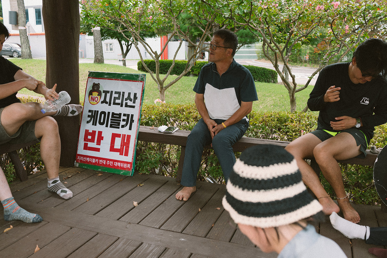 정자에 몇몇 사람들이 둘러 앉아 있다. 난간에 '지리산 케이블카 반대'라고 적힌 피켓이 기대어져 있다.