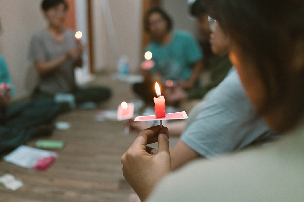 몇몇 사람들이 실내에 둘러앉아 한 손에 작은 초를 들고 있는 모습을 촬영한 사진이다. 사진의 촛점은 가장 가까운 곳에 앉은 사람이 들고 있는 초에 맞추어져 있어서 나머지 사람들의 모습은 흐리게 보인다. 촛점이 맞춰진 초는 작은 곰인형의 모습을 하고 있다. 