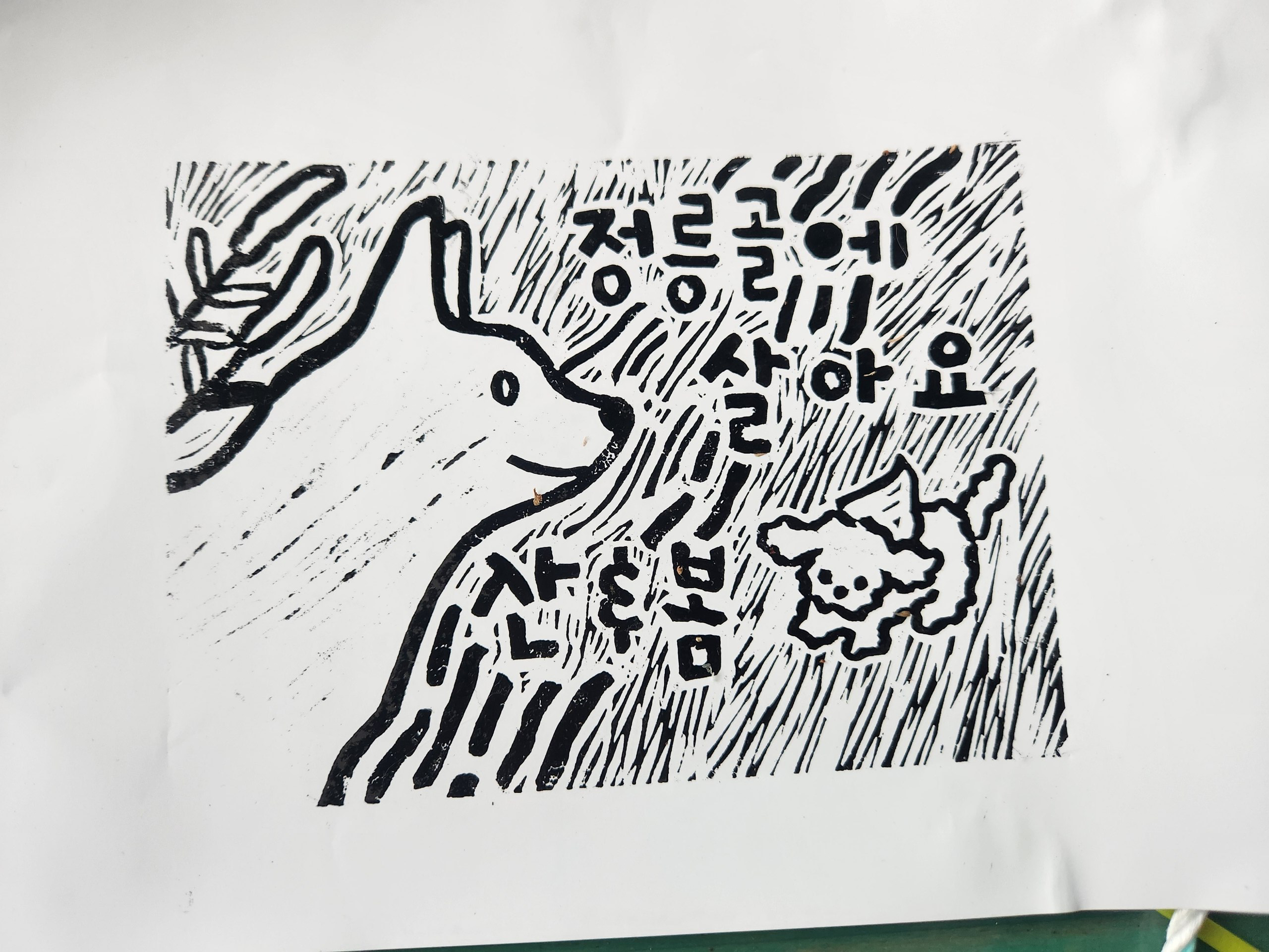 흰 종이에 검은색 잉크로 찍은 판화를 촬영한 사진이다. '정릉골에 살아요. 산&봄'이라는 문구와 두 강아지와 강아지 풀의 모습이 표현되어 있다. 