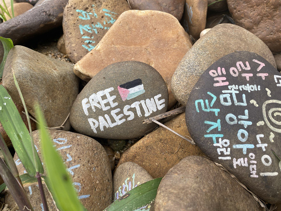 풀과 모래가 있는 바닥 위에 여러 메시지를 쓴 자갈들이 겹쳐져 놓여있다. 가운데 있는 자갈에는 팔레스타인 국기와 'FREE PALESTINE'이라는 문구가 적혀있다. 그 옆의 자갈에는 '사랑해 금강아, 우리 이대로 함께 살자'라는 문구와 태양의 모습이 적혀있다. 