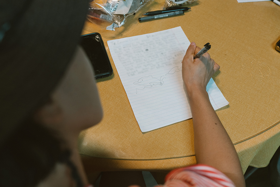 한 사람이 탁자에서 편지를 쓰는 모습을 촬영한 어깨 너머로 촬영한 사진이다. 둥근 탁자에는 노란색 식탁보와 유리가 깔려있고 주변에는 핸드폰과 과자, 펜이 놓여있다. 편지의 내용은 잘 보이지 않으며 아래쪽에 바다를 헤엄치는 돌고래의 모습이 그려지고 있다. 편지를 쓰는 사람은 검은 모자를 썼다. 