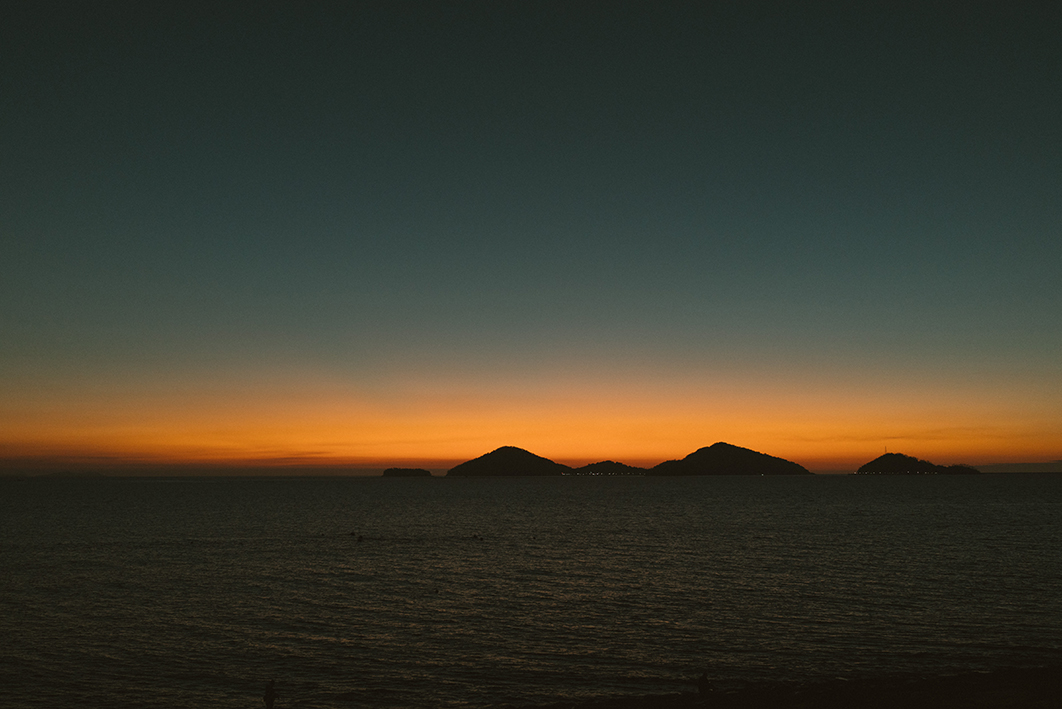 멀리 섬이 보이는 바다쪽으로 노을이 보이는 풍경을 촬영한 사진이다. 노을은 약간 남아있고 위쪽 하늘은 많이 어둡다.